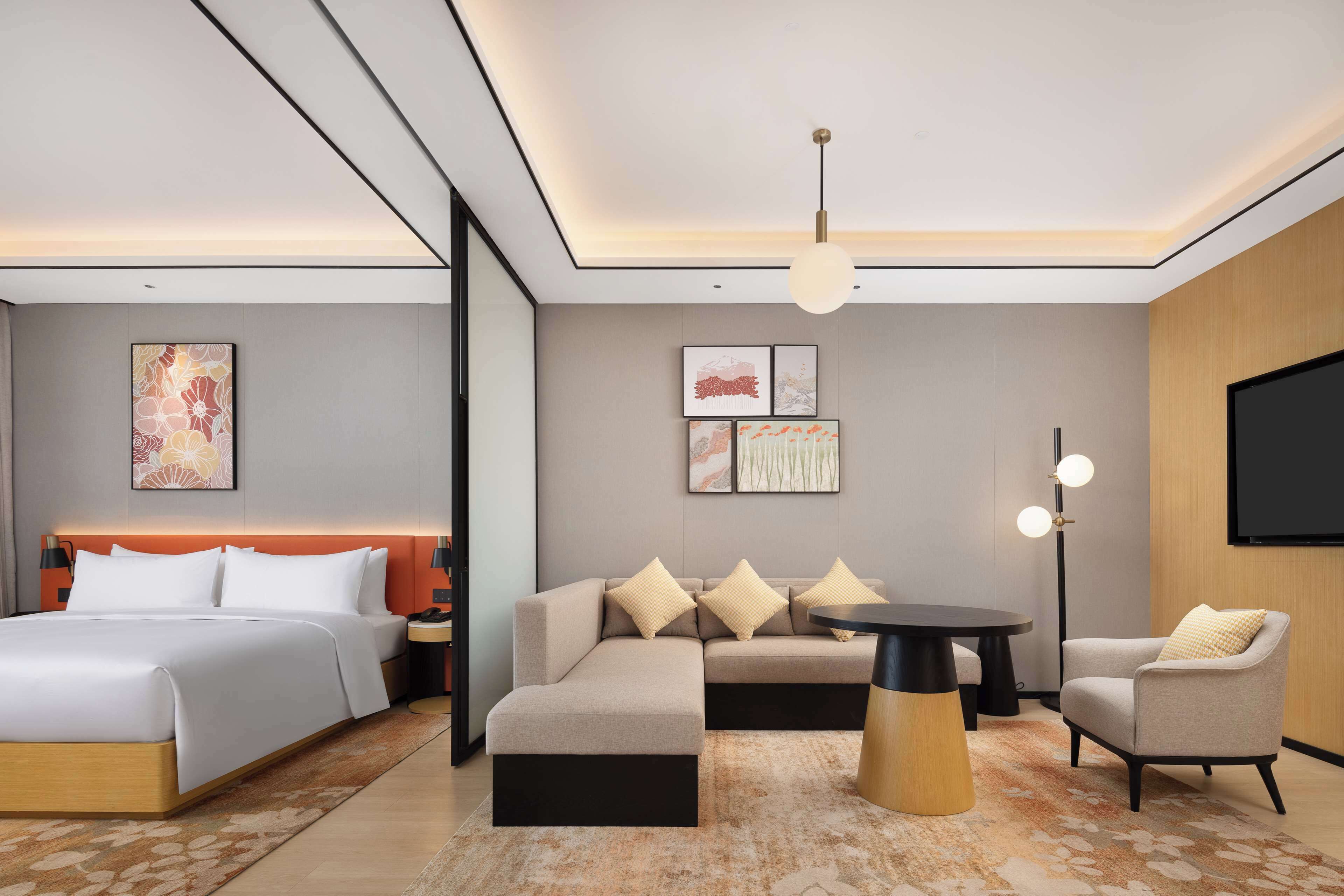 Una habitación de hotel moderna con cama, sofá, sillón y una pequeña mesa.