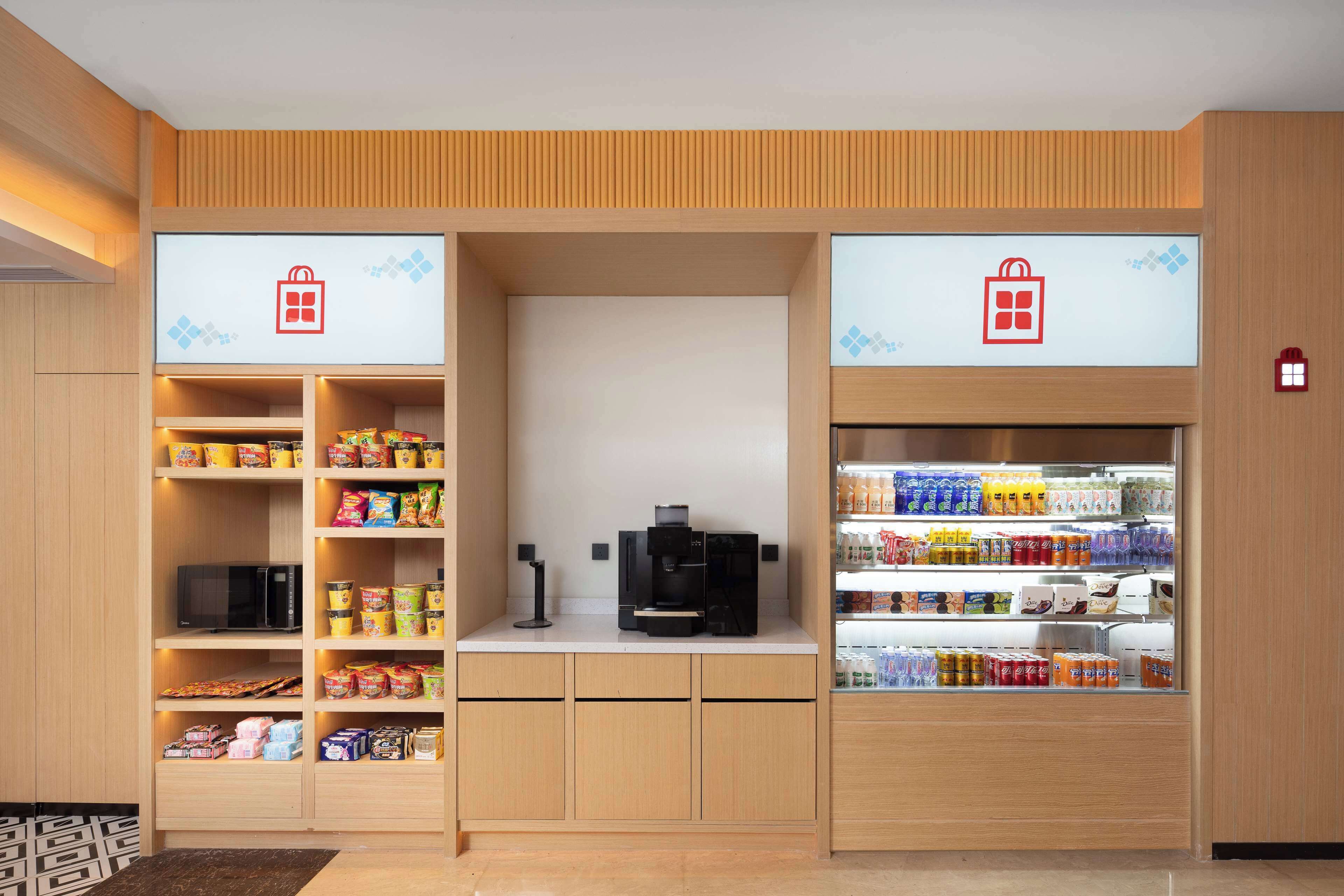 A kitchenette with a microwave, coffee maker, and shelves stocked with snacks and beverages.