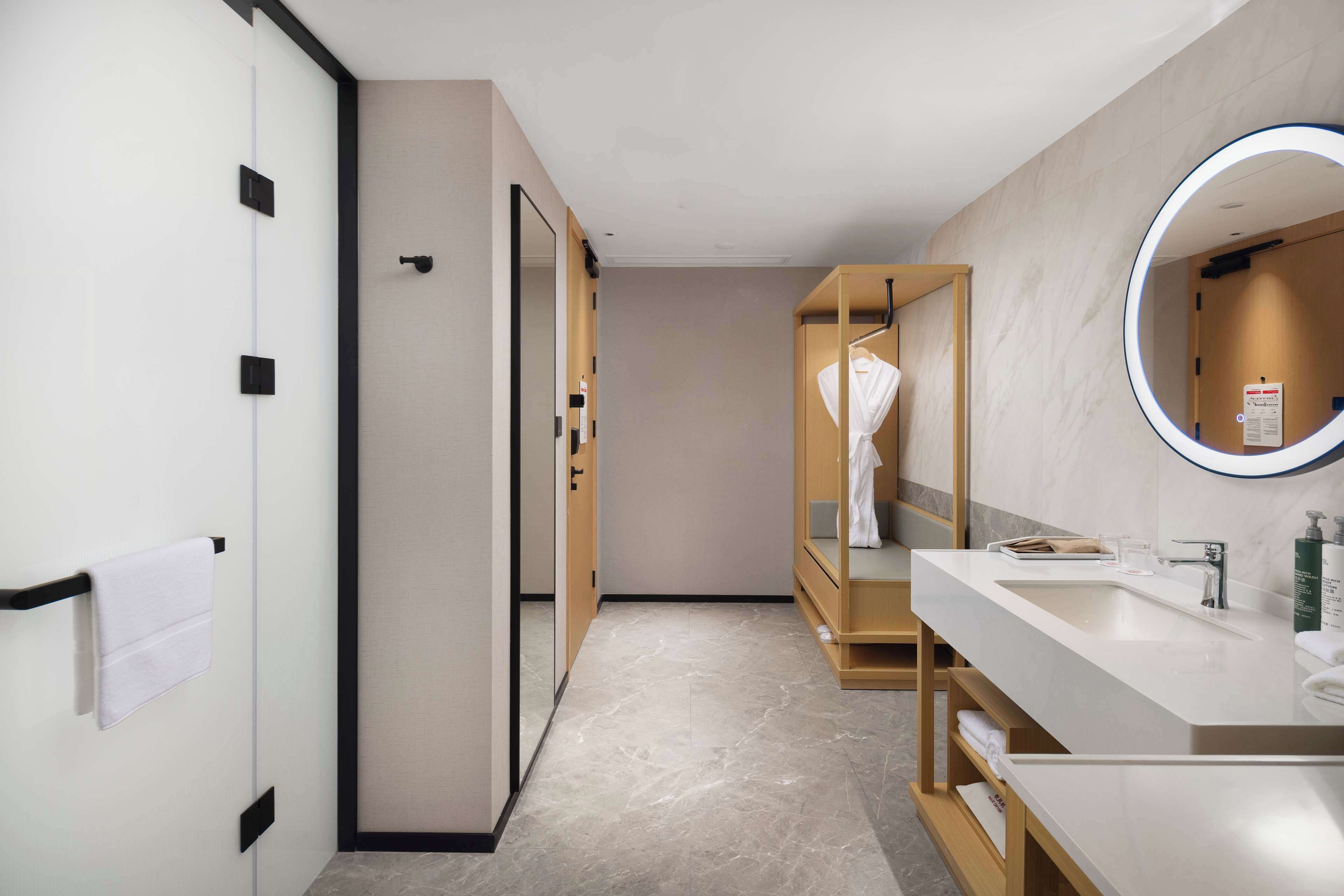 A modern bathroom with a large mirror, a sink, and a robe hanging on a wooden rack.