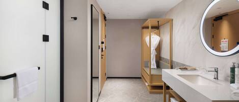 A modern bathroom with a large mirror, a sink, and a robe hanging on a wooden rack.
