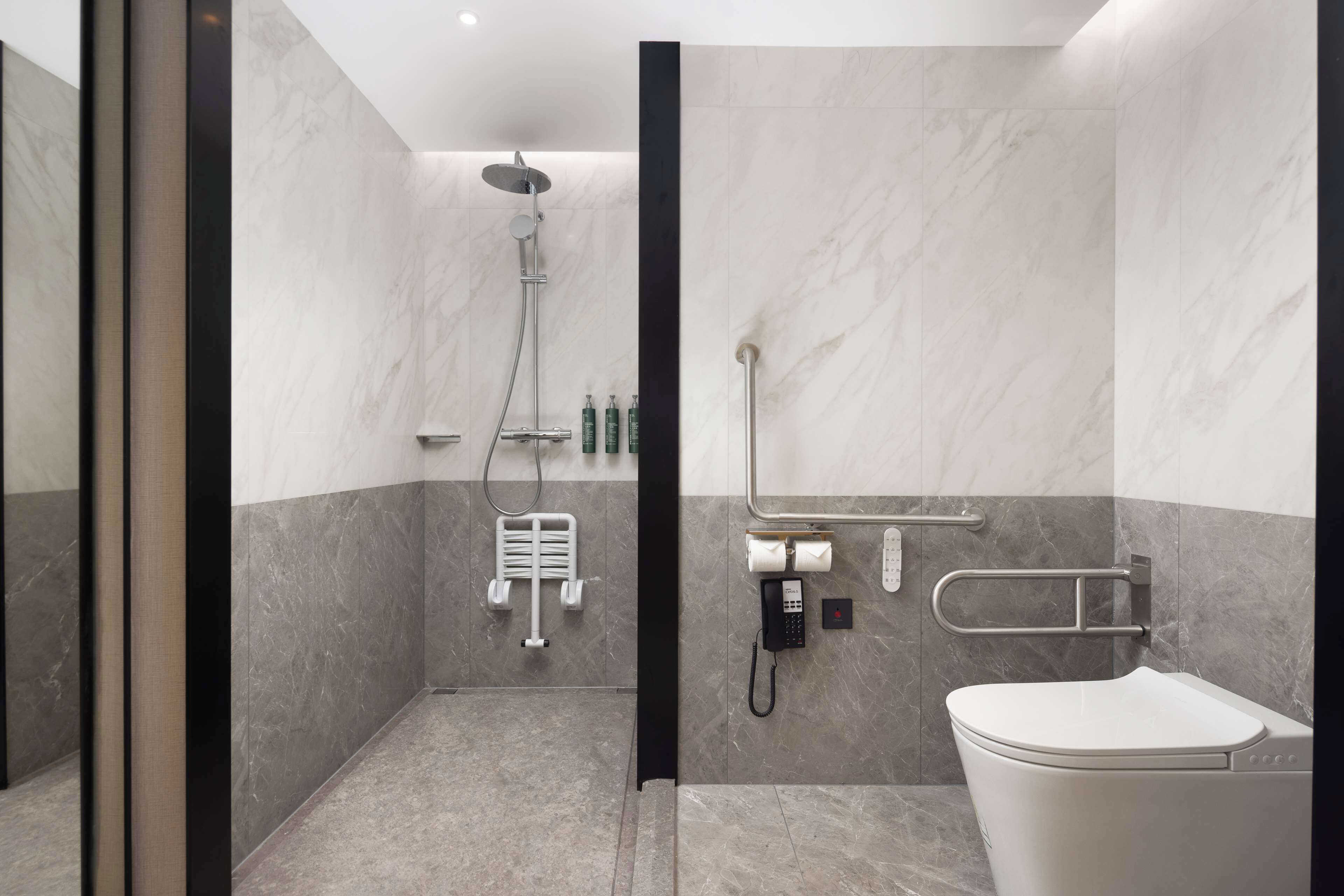 Ein modernes Badezimmer mit Dusche, Toilette und einem Handdesinfektionsmittelspender an der Wand.
