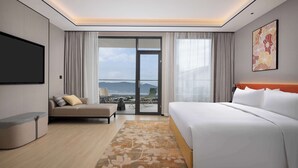 A hotel room with a bed, a sofa, a TV, and a balcony with a view. - Hilton Garden Inn Dali Ancient City (Dali)