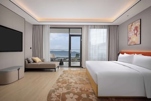 Habitación de hotel con cama, sofá, televisión y balcón con vistas.