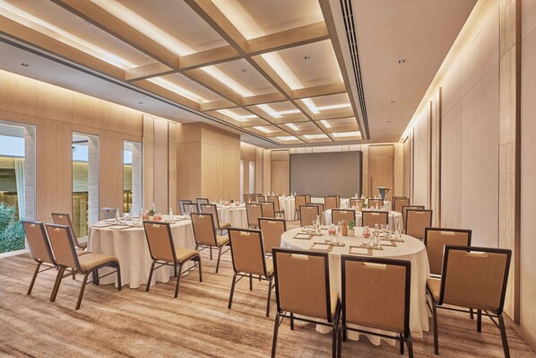 A conference room with multiple round tables, chairs, and a large screen.