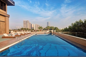 A rooftop swimming pool with lounge chairs and a view of high-rise buildings.