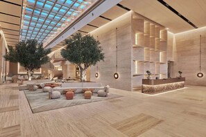 A spacious lobby with a high ceiling, large windows, and a reception desk. - Hilton Gurugram Baani City Centre (Gurugram)