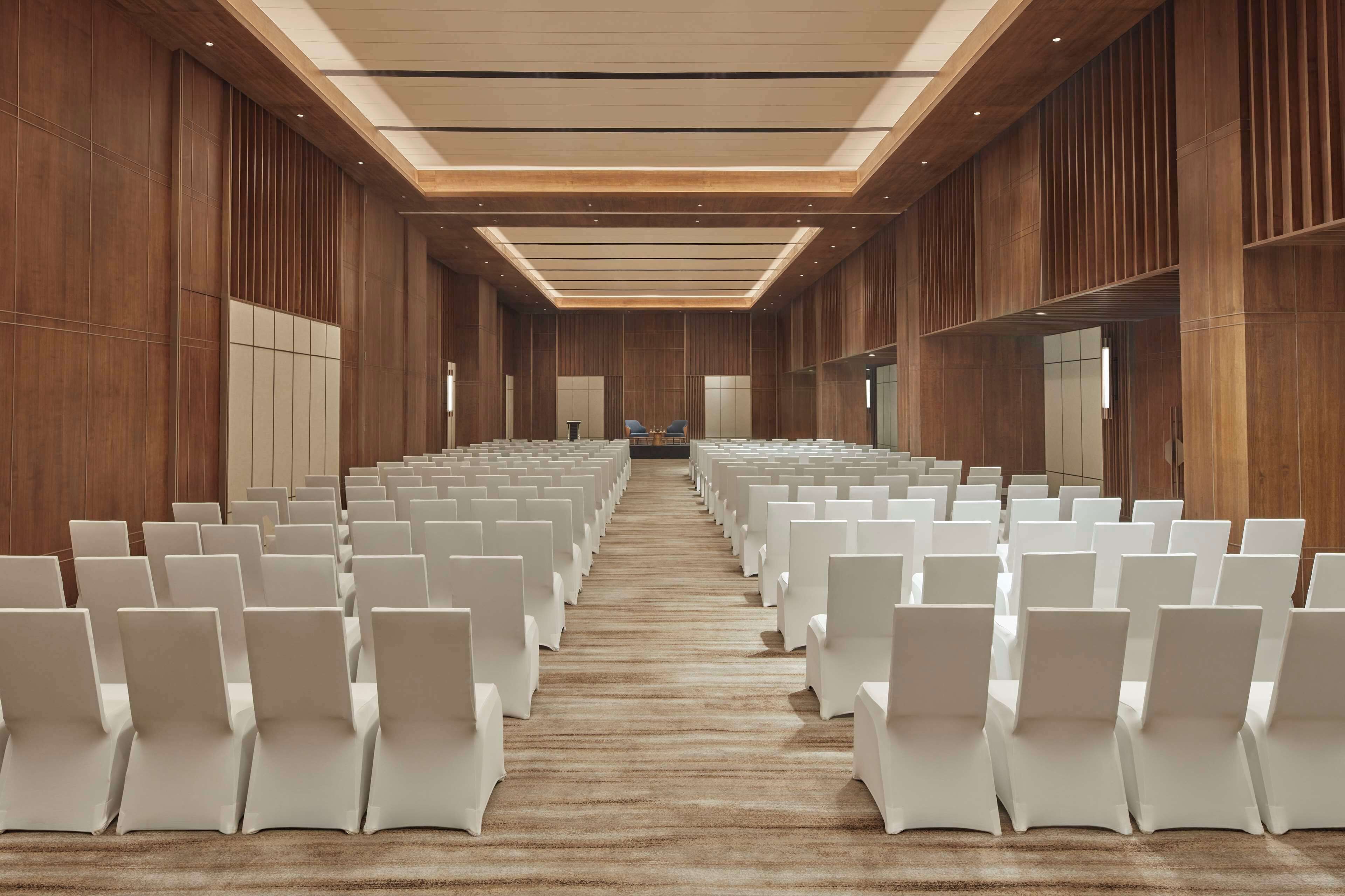 A conference room with rows of white chairs, wooden paneling, and a carpeted floor.