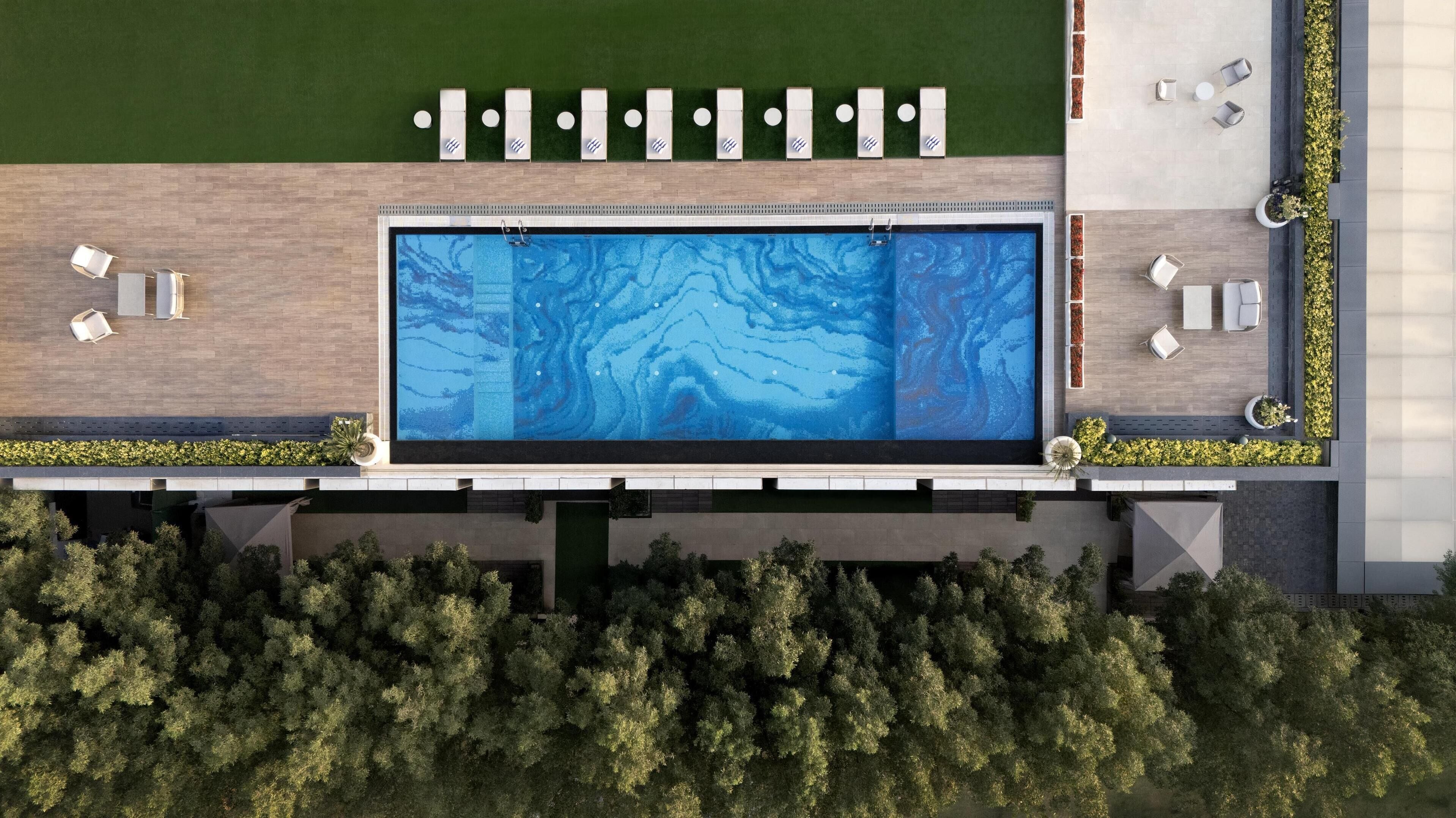 An aerial view of a modern pool area with a rectangular pool, multiple lounge chairs, and a well-maintained lawn.