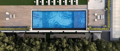 An aerial view of a modern pool area with a rectangular pool, multiple lounge chairs, and a well-maintained lawn.
