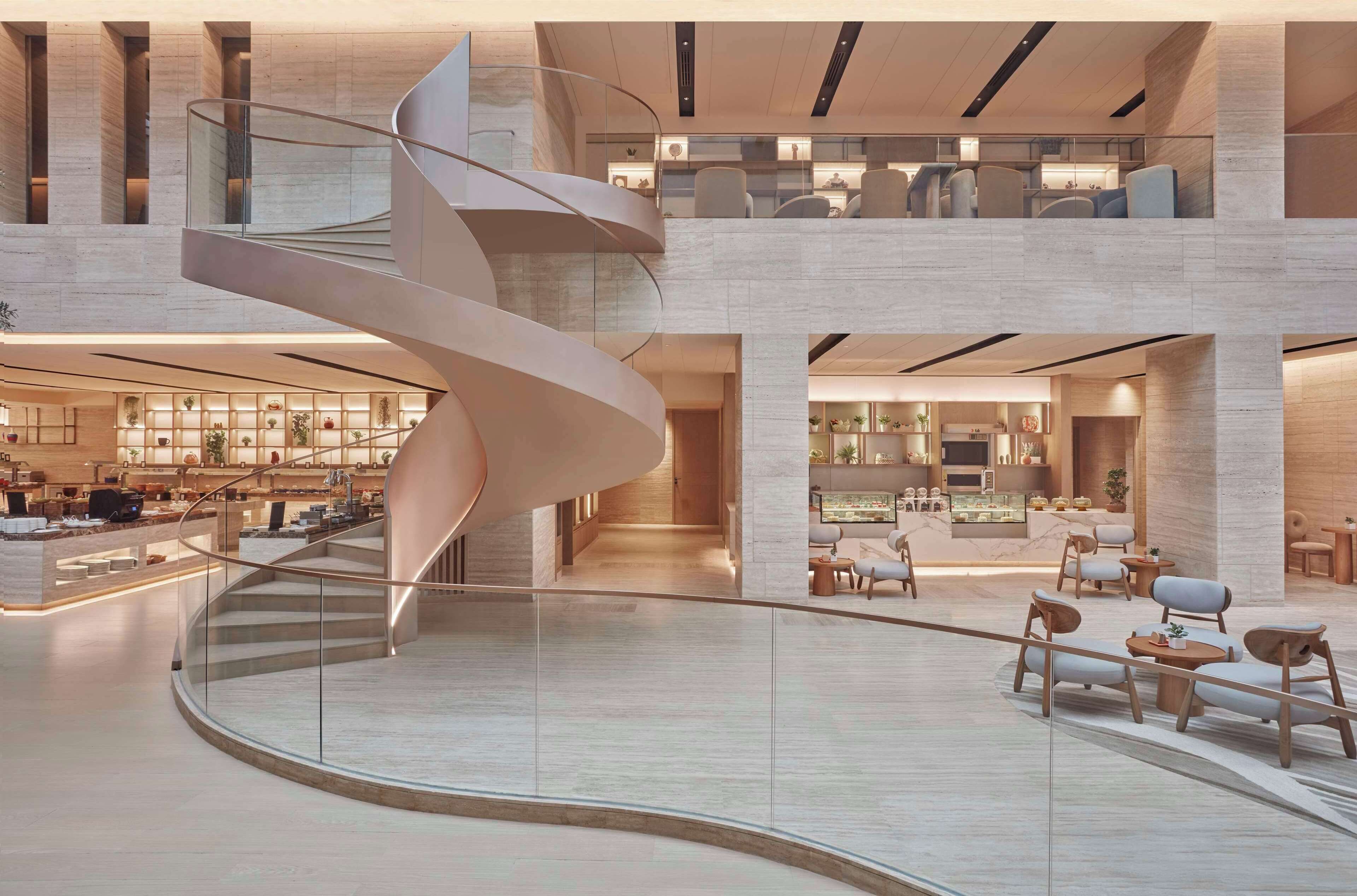 Un hall d’hôtel moderne avec un escalier en colimaçon central, des espaces de détente et un comptoir d’accueil.