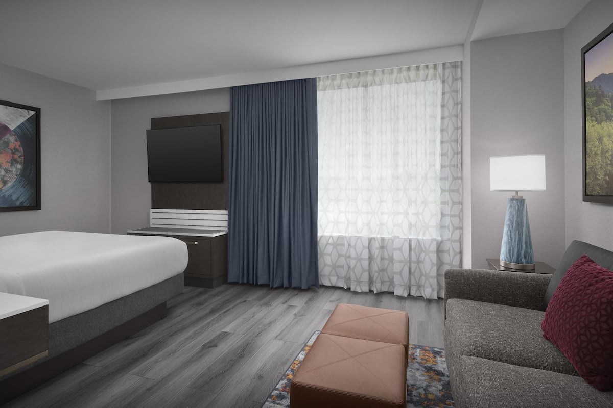 Een moderne hotelkamer met een bed, een bank, een tafeltje met een lamp en een televisie aan de muur.