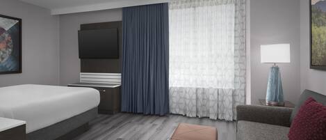 A modern hotel room with a bed, a sofa, a small table with a lamp, and a TV mounted on the wall.
