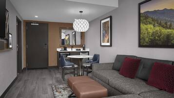 A modern living room with a grey sofa, red cushions, a brown ottoman, and a dining area with a round table and chairs.