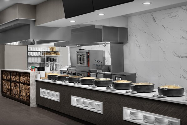 A modern kitchen with marble walls, stainless steel appliances, and a buffet counter with food dishes. - Embassy Suites By Hilton Pigeon Forge Resort (Pigeon Forge)