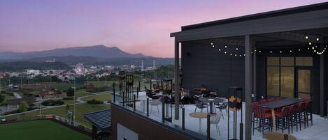 A rooftop terrace with outdoor seating, a view of a cityscape, and a mountain in the background.