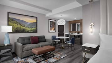 Una habitación de hotel moderna con un sofá gris, una mesita pequeña, un banco, un escritorio y una cama.