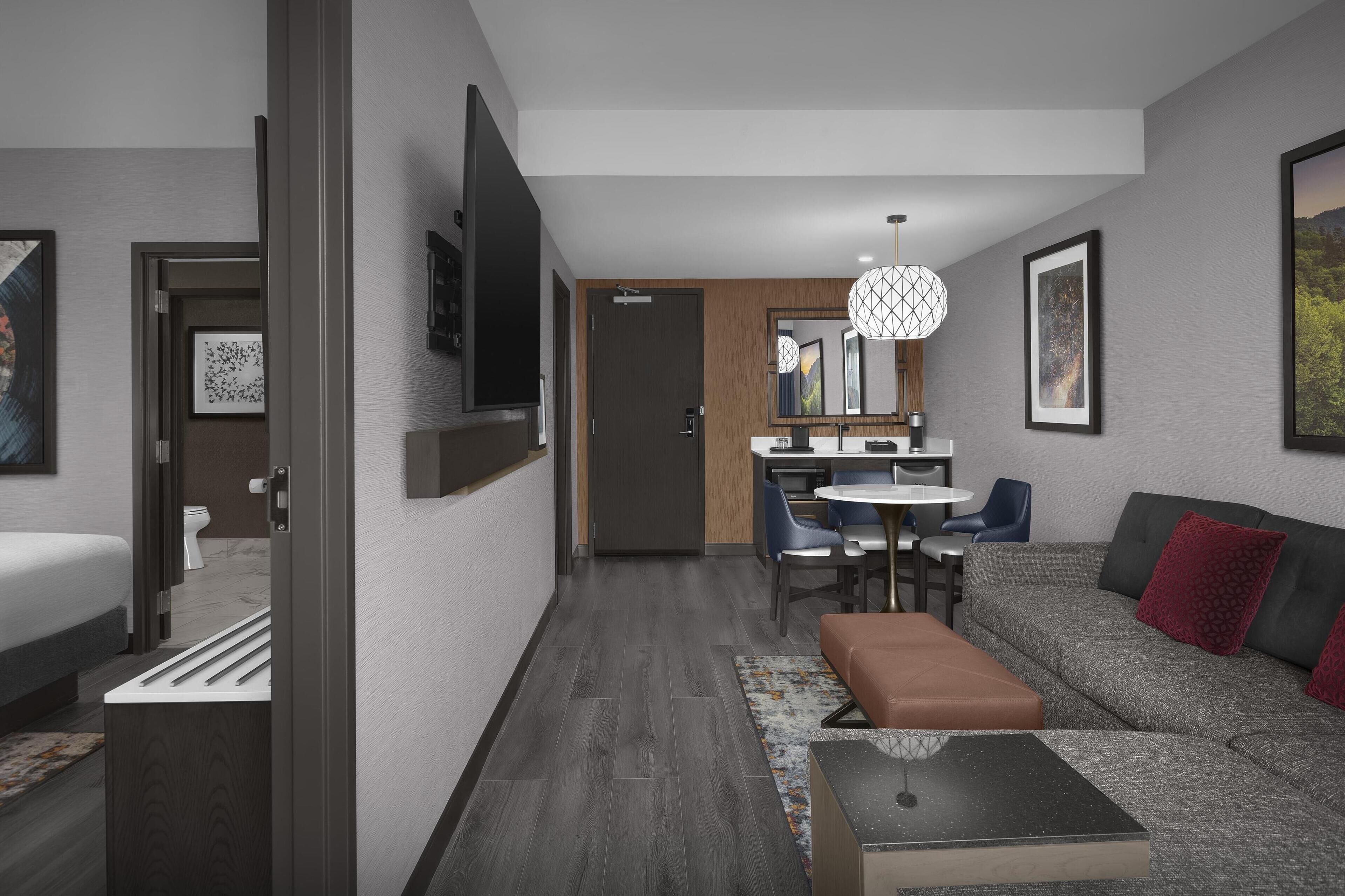 Una habitación de hotel moderna con sofá, una mesa de comedor y televisor.