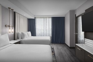 Une chambre d’hôtel moderne avec deux lits, une grande fenêtre avec des rideaux, un téléviseur à écran plat et un plancher en bois.