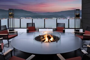 A round table with a glass fire pit in the center, surrounded by red and black chairs.