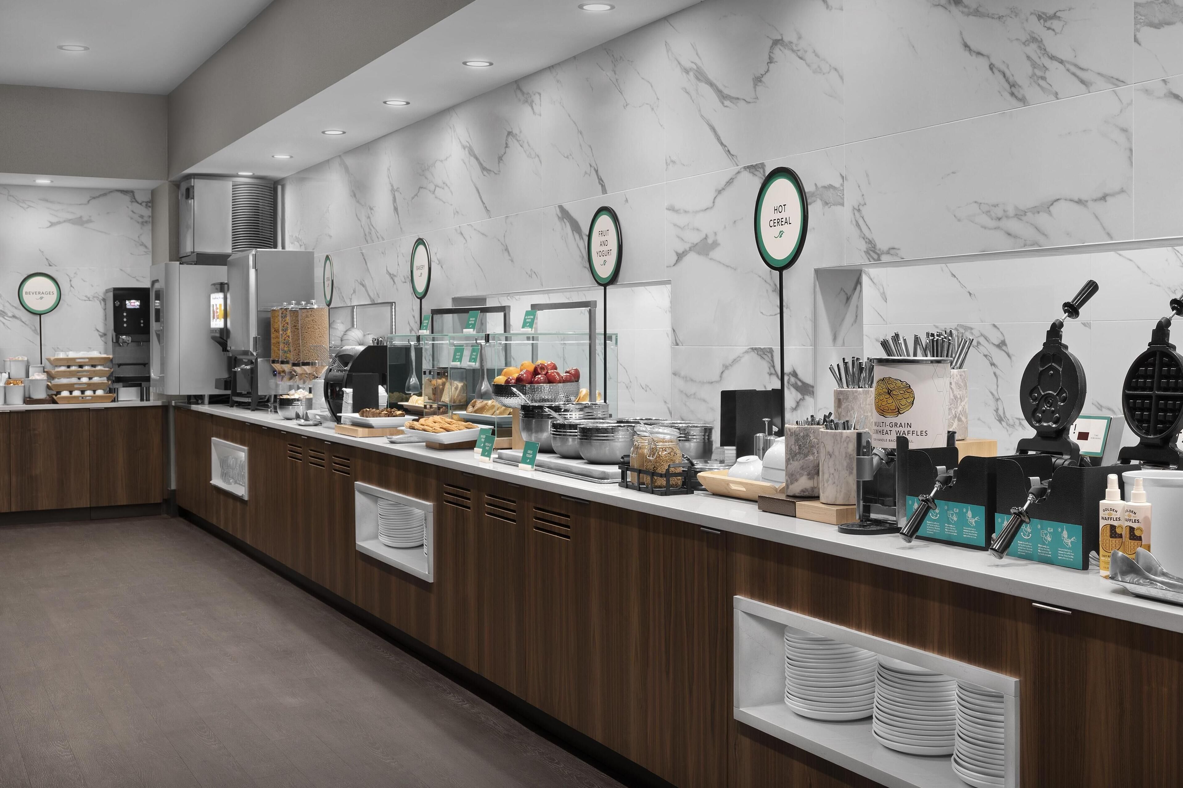 A buffet counter with various food stations, including a fruit and yogurt section, and a multi-grain waffle station.