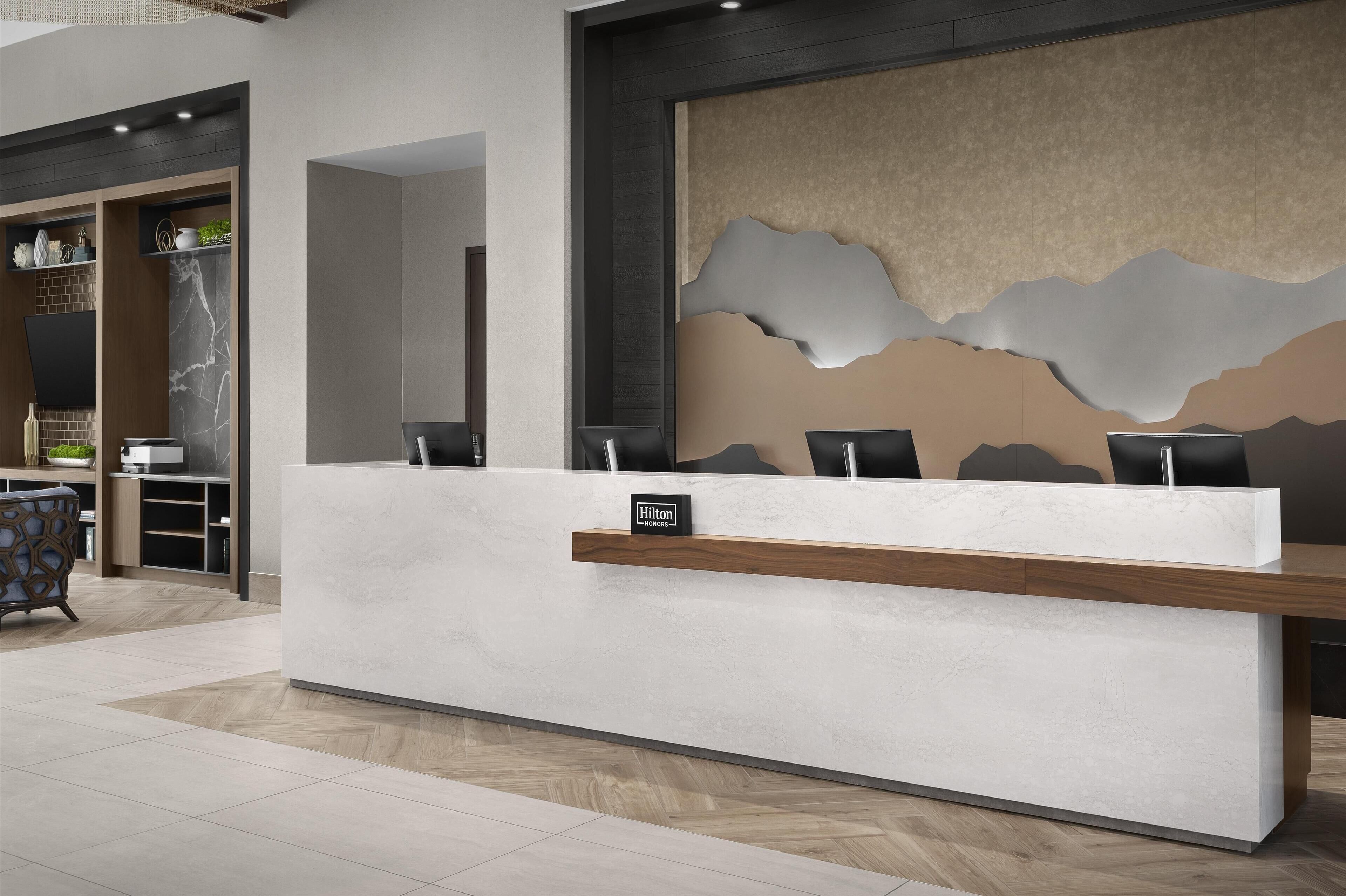 A hotel reception desk with a modern design, a wooden shelf with a sign, and a large abstract wall decoration.