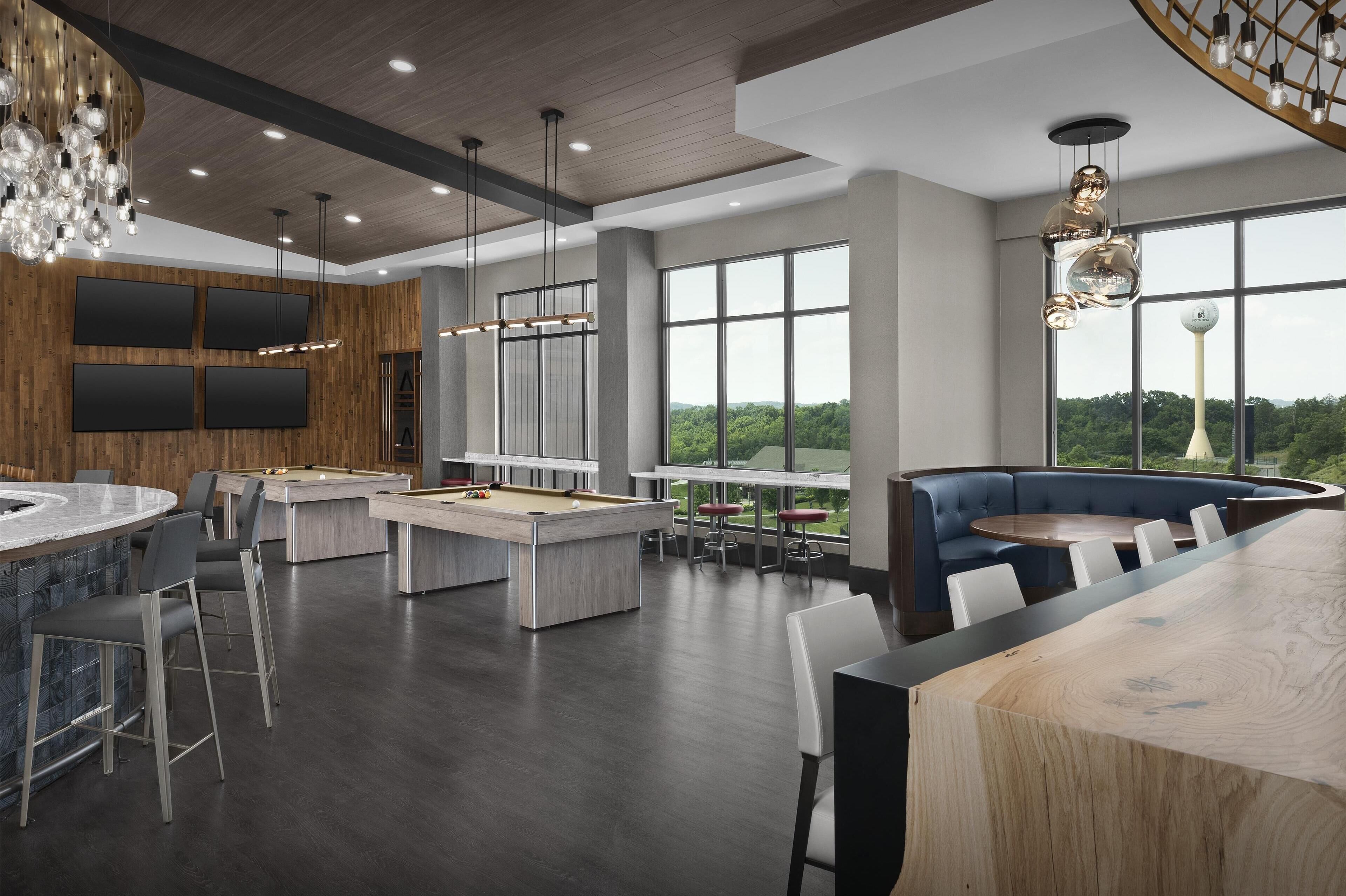 A modern lounge area with a pool table, bar seating, and a large window offering a view of the outdoors.