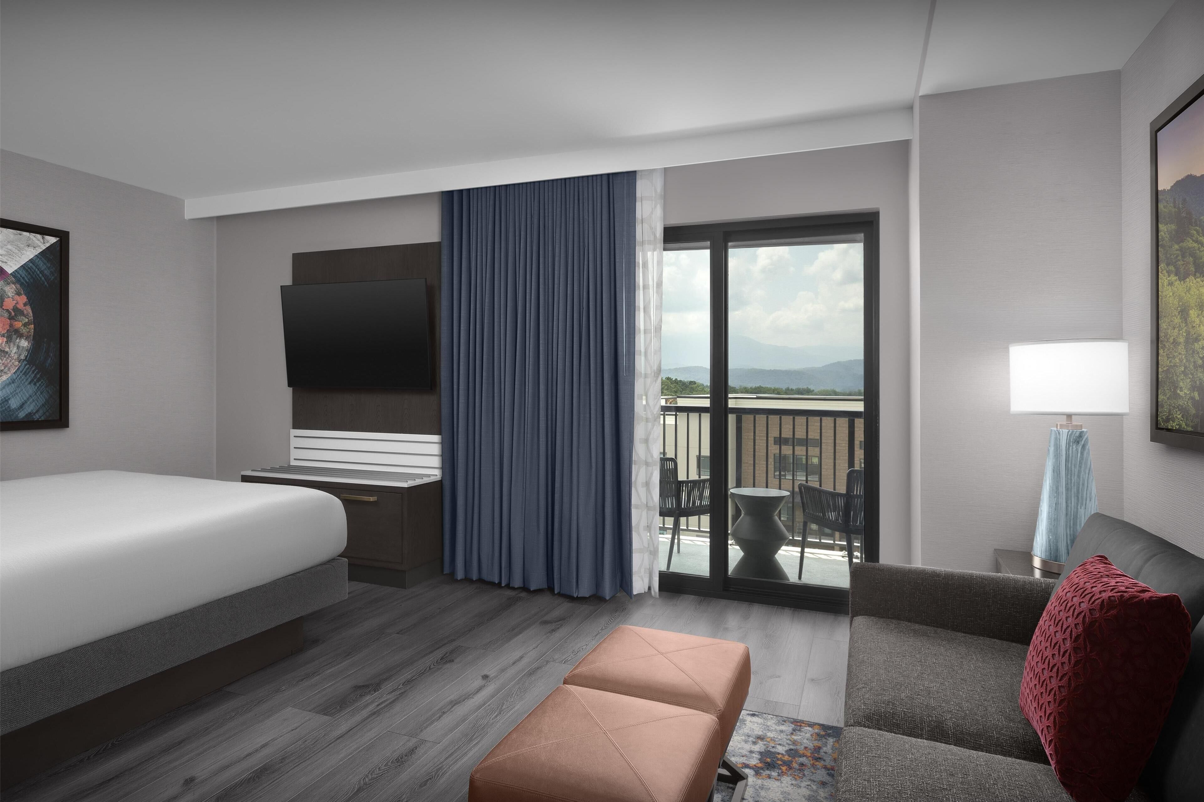 A hotel room with a bed, a sofa, a small table, a TV, and a balcony with a view.