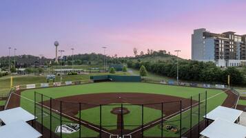 A baseball field with a large scoreboard, a tall observation tower, and a modern hotel in the background.