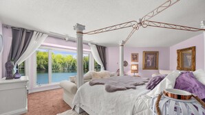 Ein Schlafzimmer mit einem großen Bett, einem weißen Schminktisch, einem Nachttisch und Blick auf einen See.