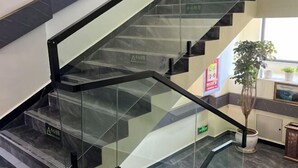 Una escalera moderna con barandillas de vidrio y escalones negros, que conduce a una zona de descanso con una planta en maceta.