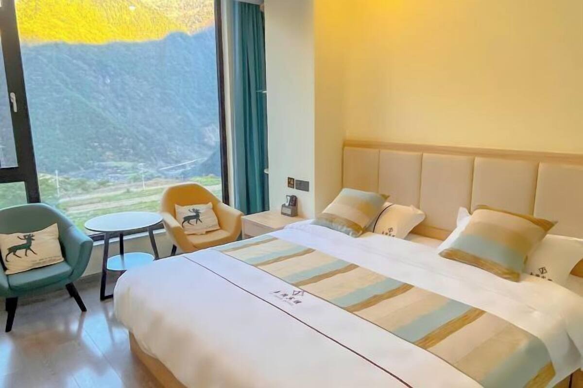 Een hotelkamer met een groot bed, een kleine tafel, twee stoelen en uitzicht op bergen door een groot raam.