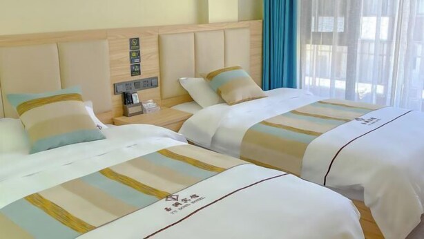 Ein Hotelzimmer mit zwei Betten, jeweils mit gestreifter Bettwäsche und einem Kopfkissen. Ein Nachttisch mit Telefon und einer kleinen Tischplatte ist vorhanden.
