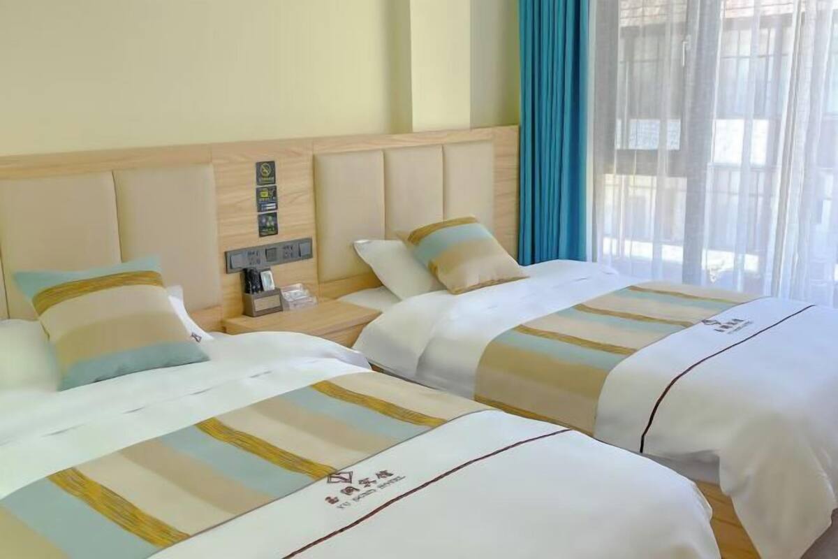 Een hotelkamer met twee bedden, elk voorzien van gestreept beddengoed en een kussen. Er staat een nachtkastje met een telefoon en een klein tafeltje.
