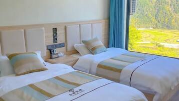 A hotel room with two beds, a nightstand, a window with a view of a green landscape, and a wooden headboard.