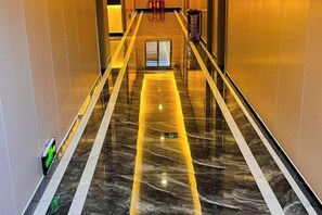 A corridor with a reflective floor, a door at the end, and a trash bin to the right. - Yudong Hotel (Gongshan)
