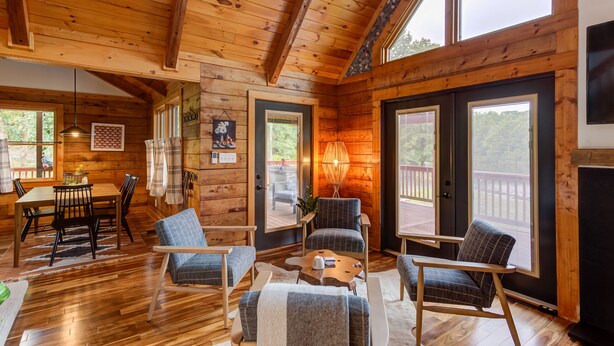 L’intérieur d’un chalet en bois comprend un coin repas, des sièges et de grandes fenêtres.