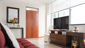 A modern living room with a red sofa, a wooden entertainment unit, a flat-screen TV, and a large window. - Elegant Surco Flat (Santiago de Surco)