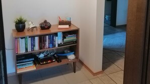 A hallway with a bookshelf containing books and decorative items, a wall-mounted light switch, and a small basket on the wall. - Gemütliche, Ruhige Ferienwohnung in Waldreicher Umgebung , 30 km bis Heidelberg (Schönbrunn)