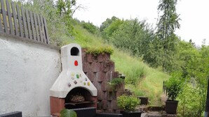An outdoor patio with wicker furniture, a brick oven, and potted plants. - Gemütliche, Ruhige Ferienwohnung in Waldreicher Umgebung , 30 km bis Heidelberg (Schönbrunn)