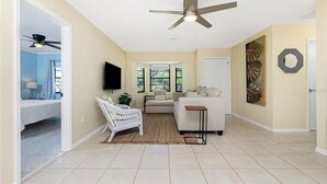 A spacious living room with a ceiling fan, a sofa, a white armchair, and a TV mounted on the wall. - Charming villa with 2 bedrooms, 4 miles from gulf beaches. Dogs welcome!  (Englewood)