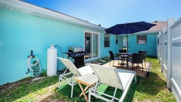 A backyard with a grill, outdoor seating, and a hose.