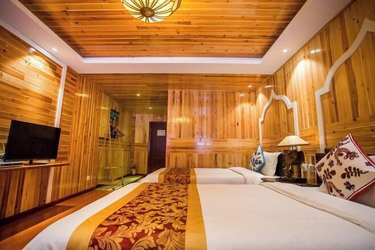 A wooden-paneled room with a television, two beds, a lamp, and a patterned bed runner.