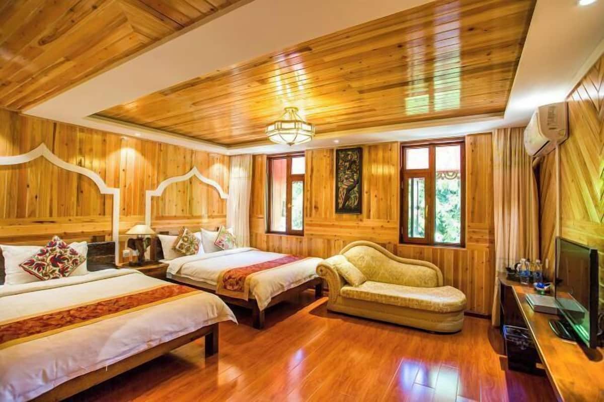 A wooden-paneled room with two beds, a sofa, a television, and a fireplace.