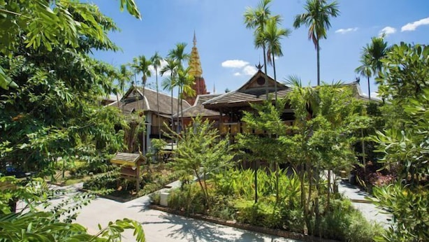 A traditional building with a thatched roof, surrounded by lush greenery and palm trees. - Meigonghe Inn (Jinghong)