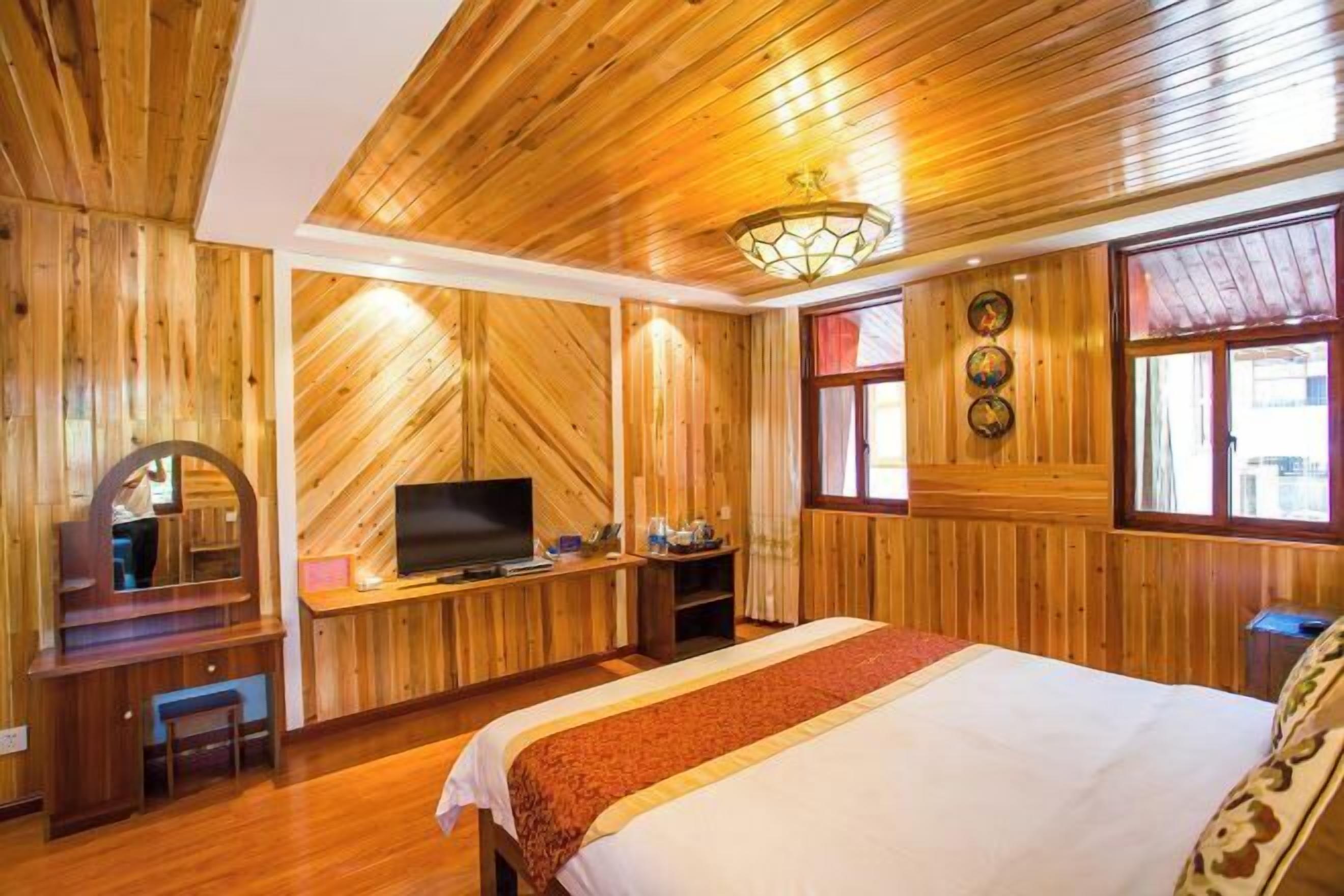 A wooden-paneled room with a bed, a television, a desk, and a mirror.