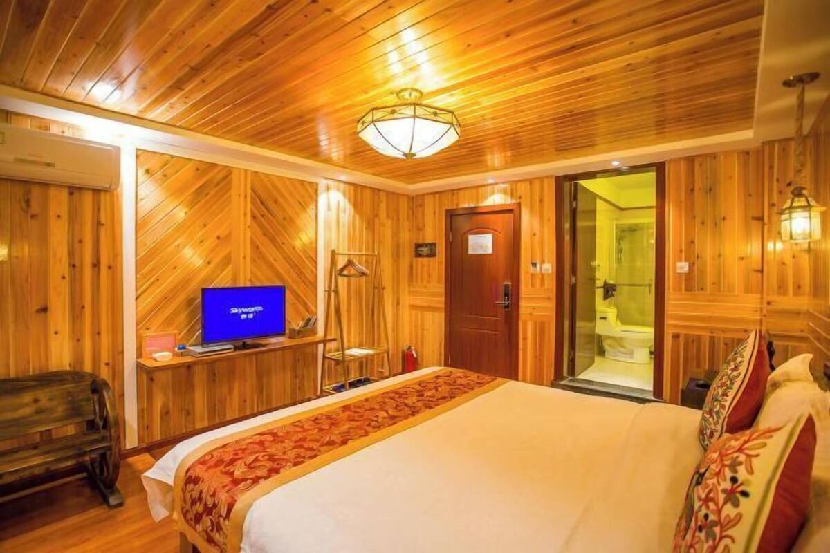 A wooden-paneled room with a bed, a television, a door leading to a bathroom, and a wooden bench.