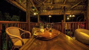 An outdoor wooden deck with a dining table, chairs, and hanging lights. - Meigonghe Inn (Jinghong)