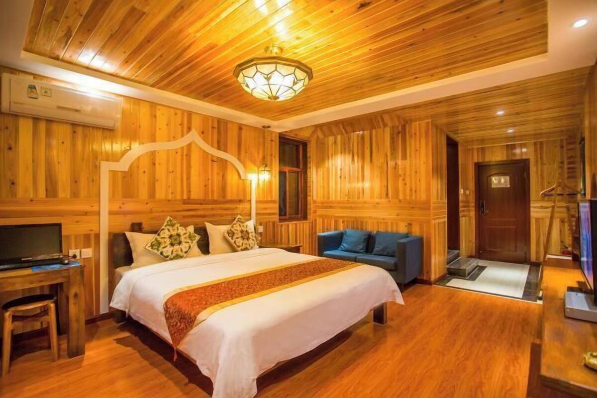 A wooden-paneled room with a bed, a sofa, a desk, and a television.