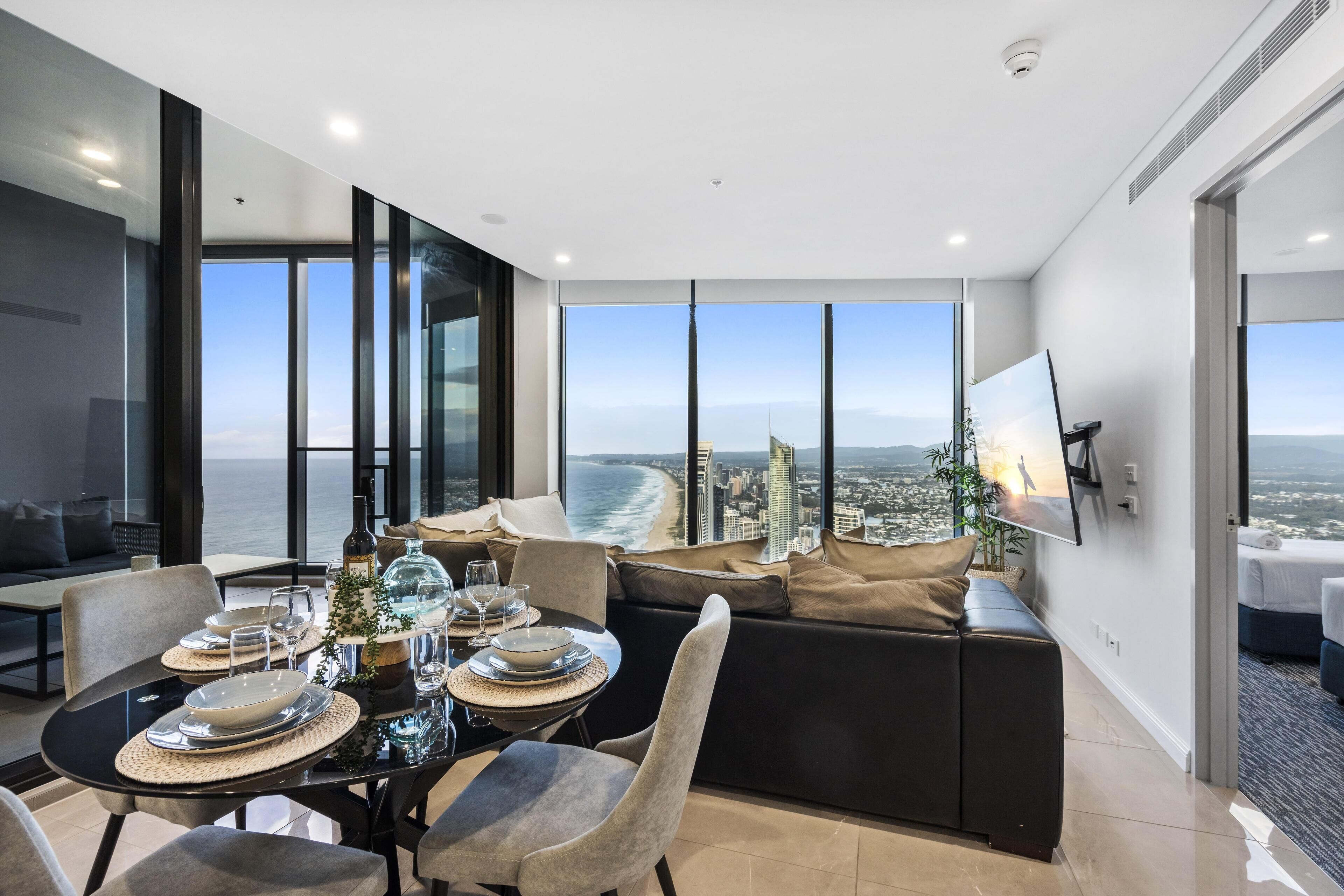 Un espace repas moderne offrant une vue panoramique sur la ville, avec un canapé et un téléviseur à écran plat fixé au mur.