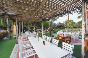 An outdoor dining area with tables and chairs, a covered seating area, and a garden with palm trees. - Naina Resort & Spa Phuket (Phuket)